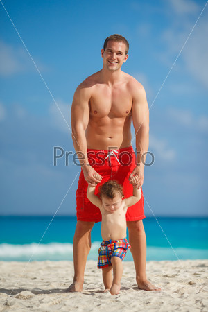Father and little son having fun on tropical white sand beach near carebbean ocean. Man with little baby boy having fun and playing near the sea water. Ocean.