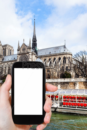 travel concept - tourist photograph cathedral Notre Dame de Paris and tourist boat in Seine River, Paris, France on smartphone with cut out screen with blank place for advertising logo