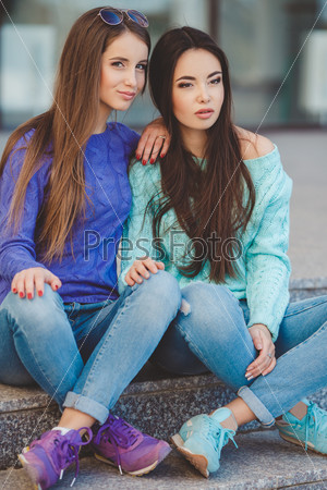 Outdoor colorful portrait of two pretty fashion girls friends dressed in urban style smiling and laughing in back light. Two young hipster girl friends together having fun. Outdoors, lifestyle.