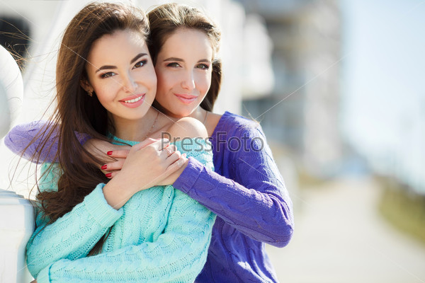Outdoor colorful portrait of two pretty fashion girls friends dressed in urban style smiling and laughing in back light. Two young hipster girl friends together having fun. Outdoors, lifestyle.