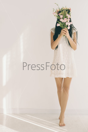 Young woman standing on tiptoes and hiding behind bouquet of flowers
