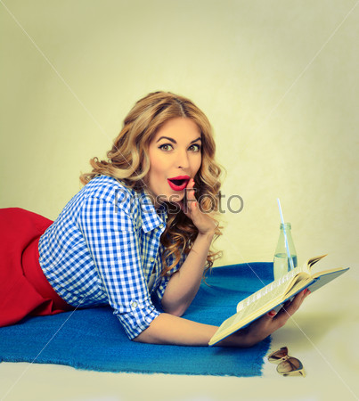 surprised blond woman reading a book lying on a plaid