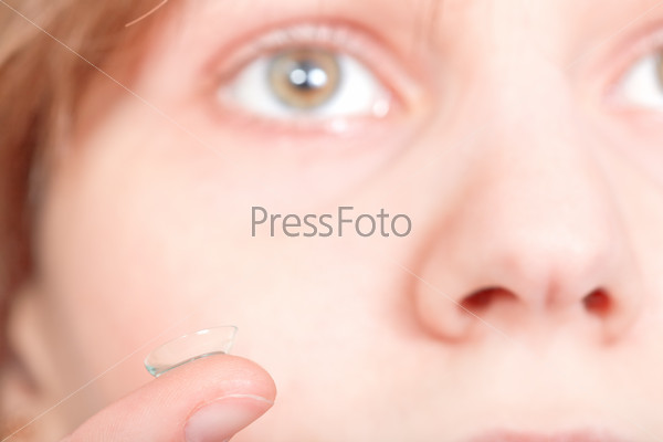 finger with contact lens in front of female face close up