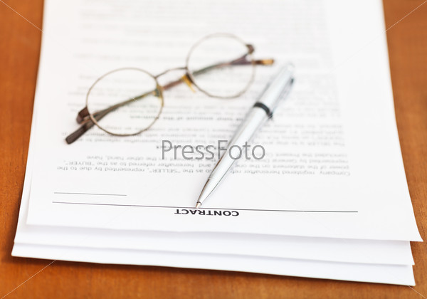 pages of sales contract and silver pen and eyeglasses on wooden table