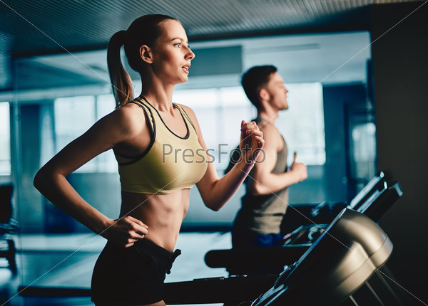 Active young woman and man running on treadmill in gym