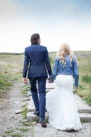Married couple taking a walk on a stepped path. Casual jacket over the bride dress.
