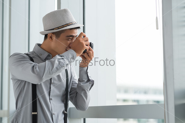 Young man in hat photographing something through window