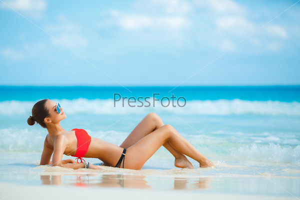 Attractive and sexy girl on the beach. Young female enjoying sunny day on tropical beach. Beautiful girl sunbathing under summer sun lying in sand on beach with blue water