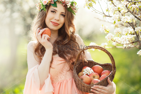 Pregnant woman posing in a green apple garden with apple in her hands. Young pregnant woman relaxing in park outdoors, healthy pregnancy. Beautiful pregnant woman holding her tummy.