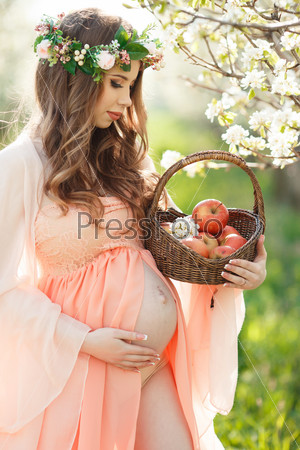 Беременная девушка в цветущем яблоневом саду