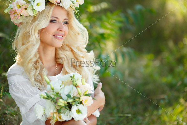 Beautiful young blonde woman in white dress and flower wreath with swing in summer outdoors. Woman outdoor. Summer portrait. Blonde girl in flowers.
