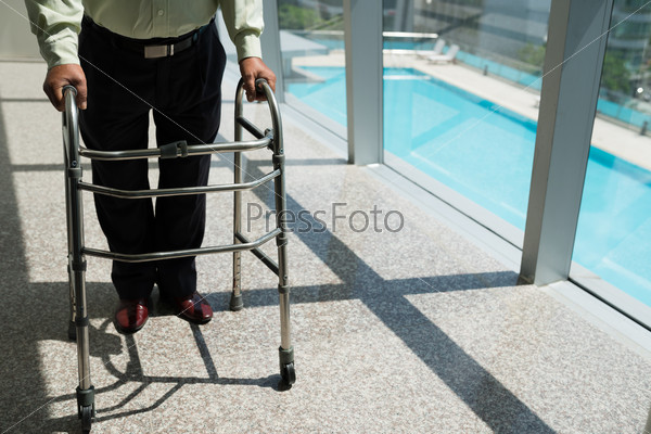Senior man walking along the corridor of hospital with walker