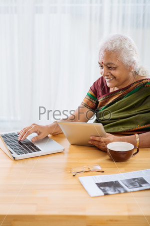 Mature Indian woman using laptop and touchpad simultaneously