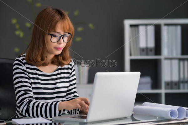 Vietnamese businesswoman sitting at table and typing text on laptop keyboard