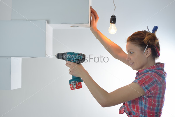 Beautiful young woman uses an electric drill