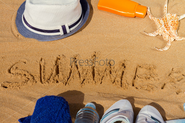 word summer written in sand white sneakers, bottle of water, suntun lotion and hat, top view