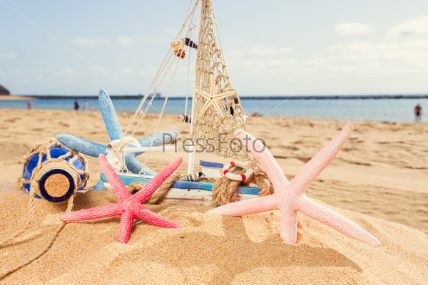 wooden model boat with seashells at ocean coast at sunny summer day