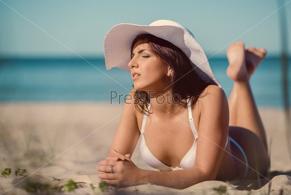 Young woman wearing white bikini and hat relaxing on the beach