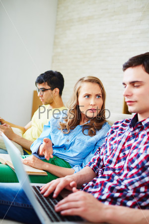 Modern guy using laptop while his girlfriend expressing displeasure with it