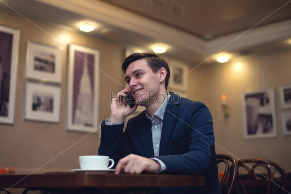 Young businessman on the phone with a smile on his face and a cup of cofee in front of him.