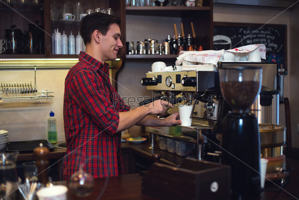 Young handsome barista hipster making coffee for his clients in the cafe