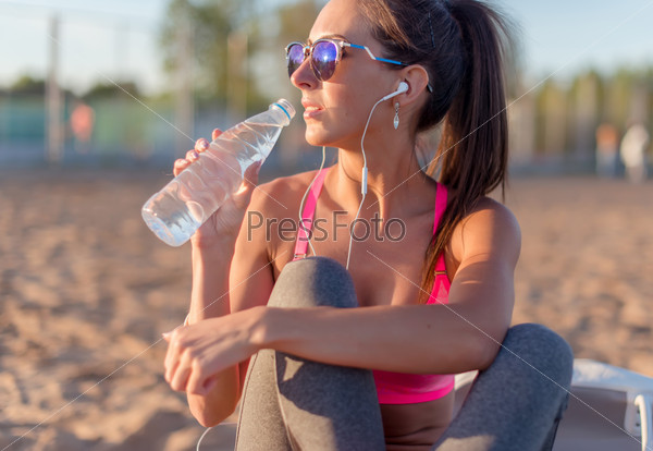 Beautiful fitness athlete woman drinking water after work out exercising on summer in beach outdoor portrait