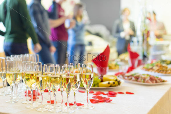 Banquet event. Table with the wineglasses, snacks and cocktails. People celebrating in the background.