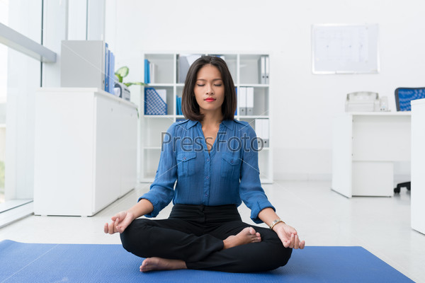 Calm brunette businesswoman practicing yoga in office