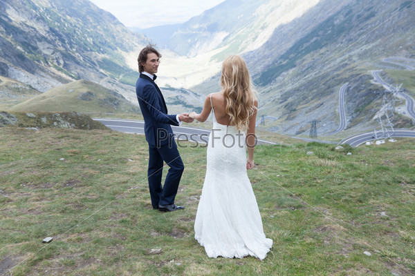 Married couple taking a walk in nature, admiring the beauty of mountains. He takes her by the hand to show the beautiful view.