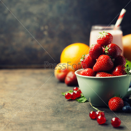 Strawberries in a cup, smoothie and fresh fruits on rustic background