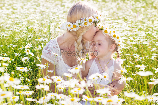 Happy family mother with cute little child girl in the chamomile field in spring