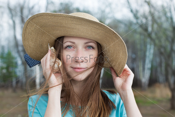 Happy girl in hat listening seashell on a windy day