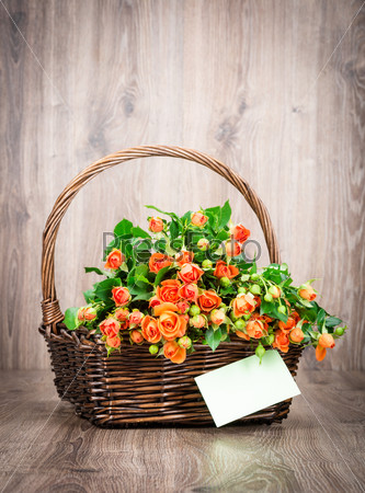 Roses in the basket and a greeting card on wooden background