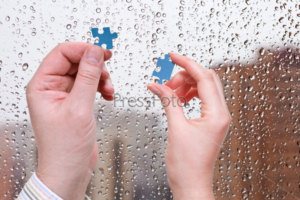male and female hands with little puzzle pieces with home window and rain drops background