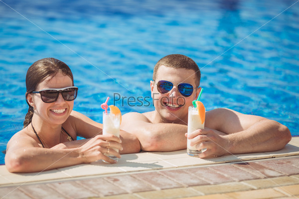 Beautiful couple drinking cocktails, hugging and kissing in the swimming pool on tropical resort