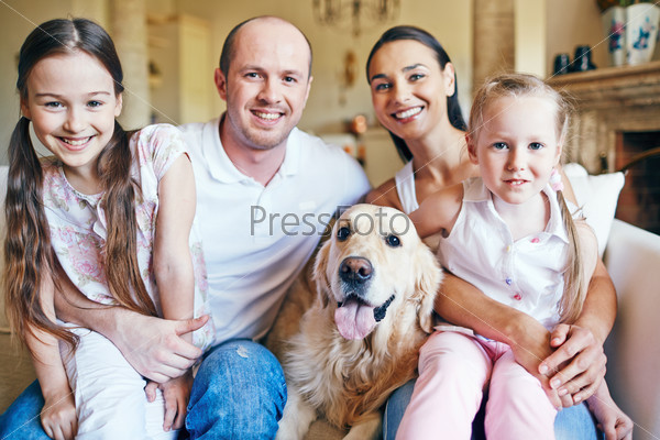 Cute siblings sitting on knees of their parents with dog near by