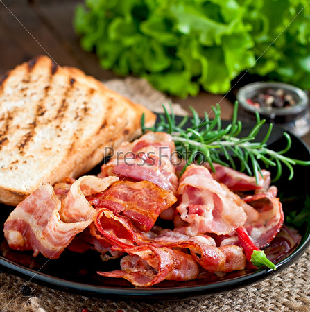 Fried bacon and toast on a black plate on a wooden background