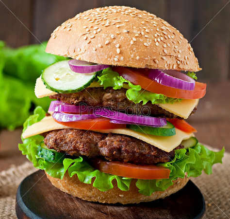 Big juicy hamburger with vegetables and beef on a wooden background in rustic style