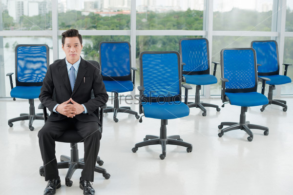 Successful serious manager sitting on a chair in modern office