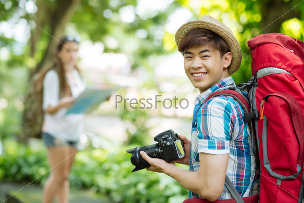 Portrait of cheerful Vietnamese tourist with large backpack and digital camera