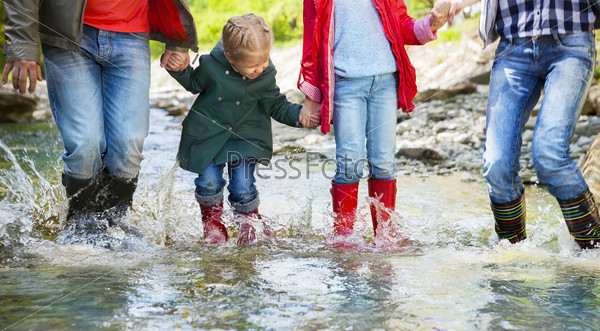 Happy family with two children wearing rain boots jumping into a mountain river. Photo in motion. DOF