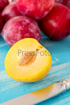 Half yellow plum on blue wooden board, with large group of red plums on background