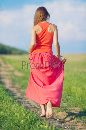 Portrait of young beautiful woman in long red dress standing back on the road in the field outdoor