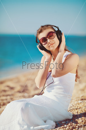 Portrait of beautiful woman sitting on the beach near the sea in headphones listening to music