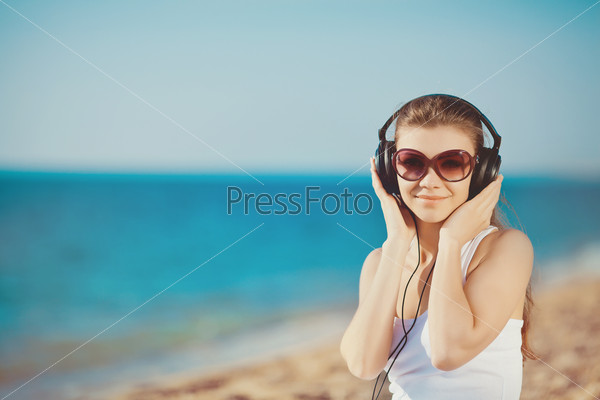 Portrait of beautiful woman sitting on the beach near the sea in headphones listening to music