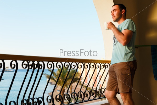 handsome guy standing on balcony in luxury hotels in Egypt at sunset and drinking tea.