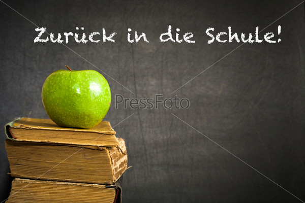 Green apple on old book against blackboard with text \