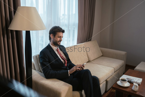 Businessman sitting on the sofa and reading message on his phone