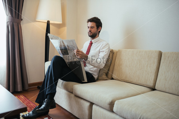 Serious businessman sitting on the sofa and reading newspaper