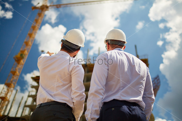 Male architects in helmets discussing new construction while standing in front of it